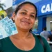 Mulher segura notas de R$ 100 em frente a uma agência da Caixa, representando o pagamento do Bolsa Família de outubro.