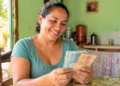 Mulher segura dinheiro em casa, representando o pagamento de R$ 1.200 do programa Mães de Pernambuco.