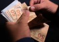 Mãos contando cédulas de cinquenta reais, representando o valor do seguro-defeso pago aos pescadores artesanais.