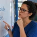 Professora aponta para as palavras “tireoide” e “tiroide” escritas em um quadro branco.