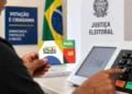 Pessoa segurando cartão do Bolsa Família em seção eleitoral com urna eletrônica ao fundo