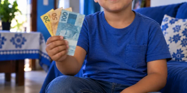 Criança segurando notas de dinheiro brasileiro em ambiente doméstico, representando a pensão especial destinada a filhos de vítimas de feminicídio.