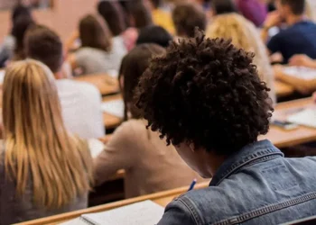 Estudantes sentados em carteiras durante aplicação de prova em sala de aula.