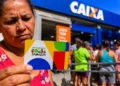 Beneficiária segura cartão do Bolsa Família em frente a uma agência da Caixa, em contexto de possível manutenção dos valores em 2027.