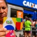 Beneficiária segura cartão do Bolsa Família em frente a uma agência da Caixa, em contexto de possível manutenção dos valores em 2027.