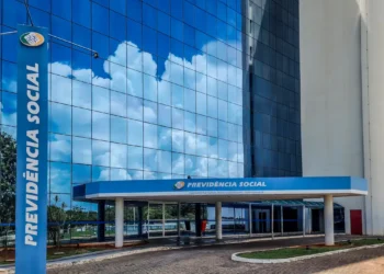 Fachada envidraçada do edifício sede da Previdência Social, com totem de identificação na entrada, órgão responsável pelo concurso do INSS.