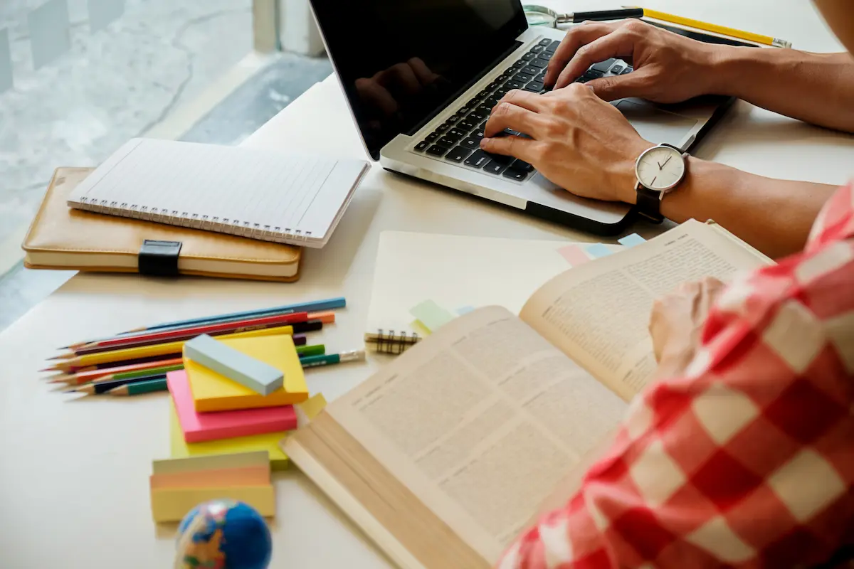 Pessoa estudando para concurso público com notebook, livros e materiais de preparação.