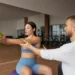 Profissional de educação física orienta mulher durante exercício com bola em academia.