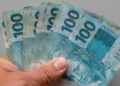 Mão segura cédulas de R$ 100 em referência aos recursos previstos no Projeto de Lei Orçamentária de 2027.