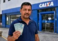 Homem segura cédulas de reais em frente a uma agência da Caixa representando o pagamento do ressarcimento do PIS/Pasep
