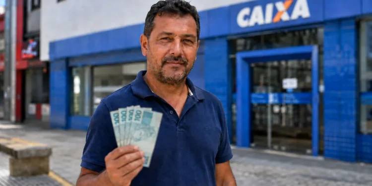 Homem segura cédulas de reais em frente a uma agência da Caixa representando o pagamento do ressarcimento do PIS/Pasep