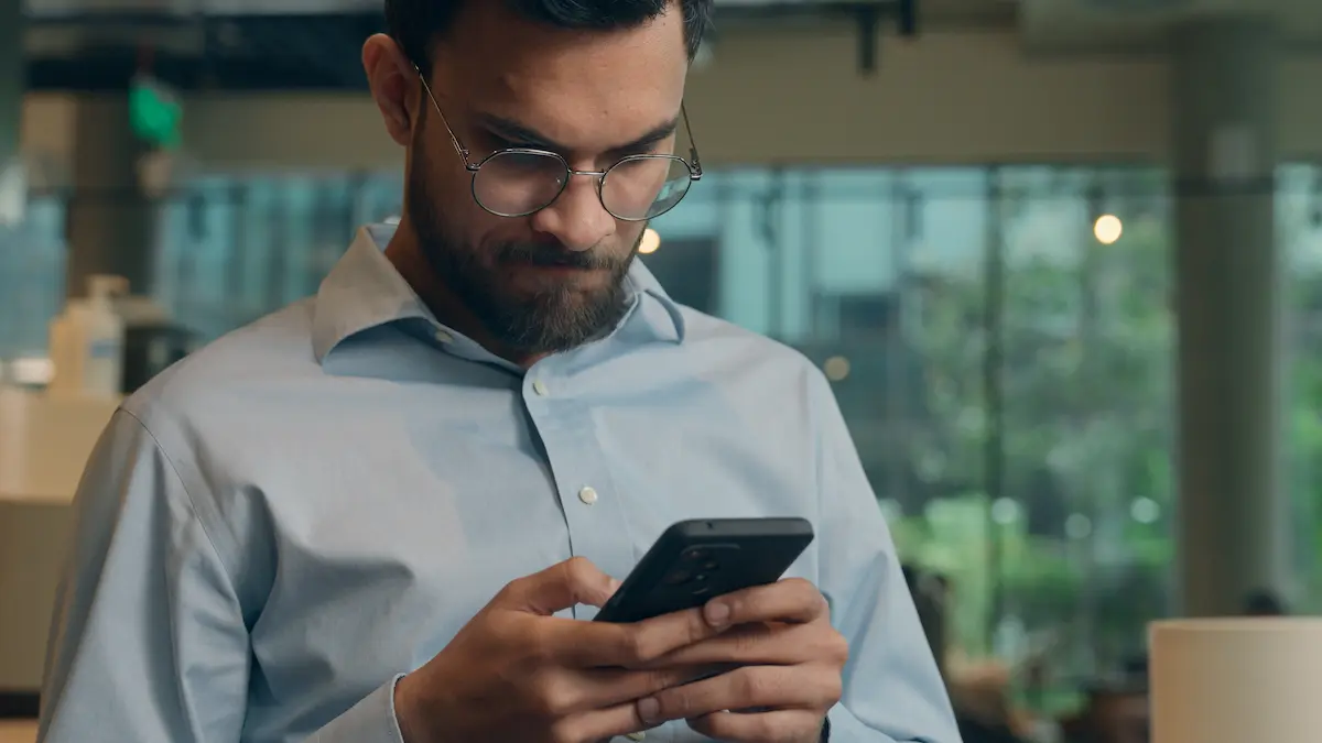 Homem consulta informações pelo celular em ambiente interno.
