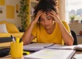 Concurseira estudando em casa, com expressão de preocupação, representando a importância da saúde mental durante a preparação para concursos públicos.
