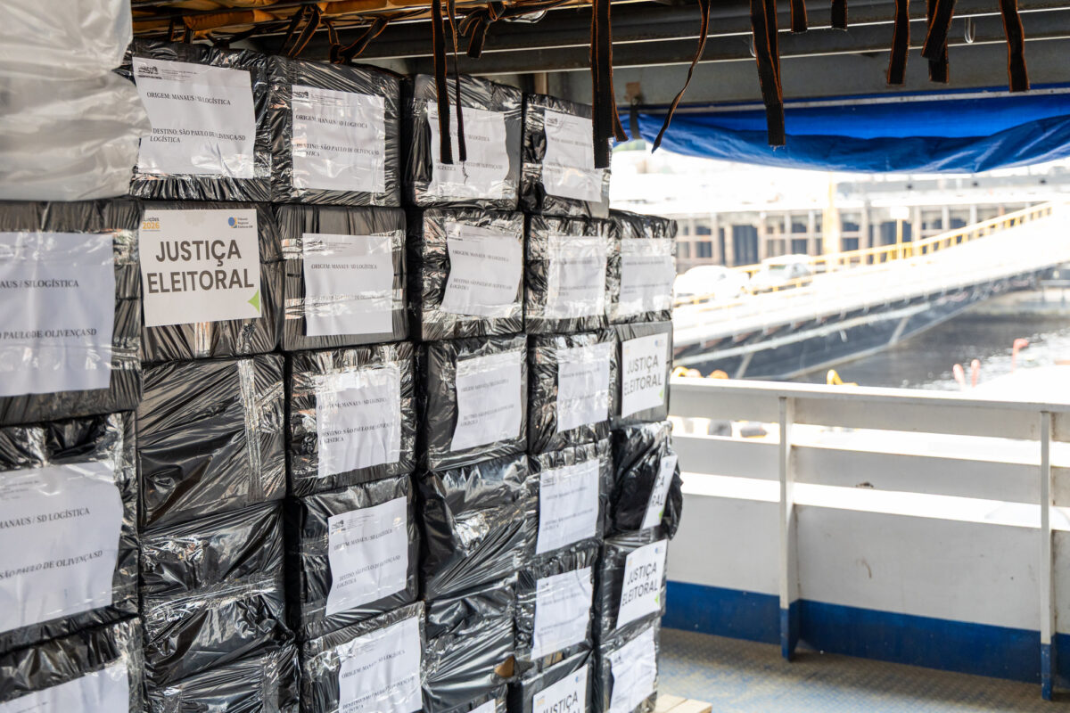 Caixas lacradas e etiquetadas com o selo da Justiça Eleitoral empilhadas no convés de uma embarcação, prontas para o transporte das urnas eletrônicas até os municípios do interior.
