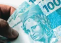 Notas de R$ 100 em mãos de segurado representam os valores atrasados do INSS liberados pela Justiça para beneficiários.