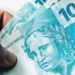 Notas de R$ 100 em mãos de segurado representam os valores atrasados do INSS liberados pela Justiça para beneficiários.